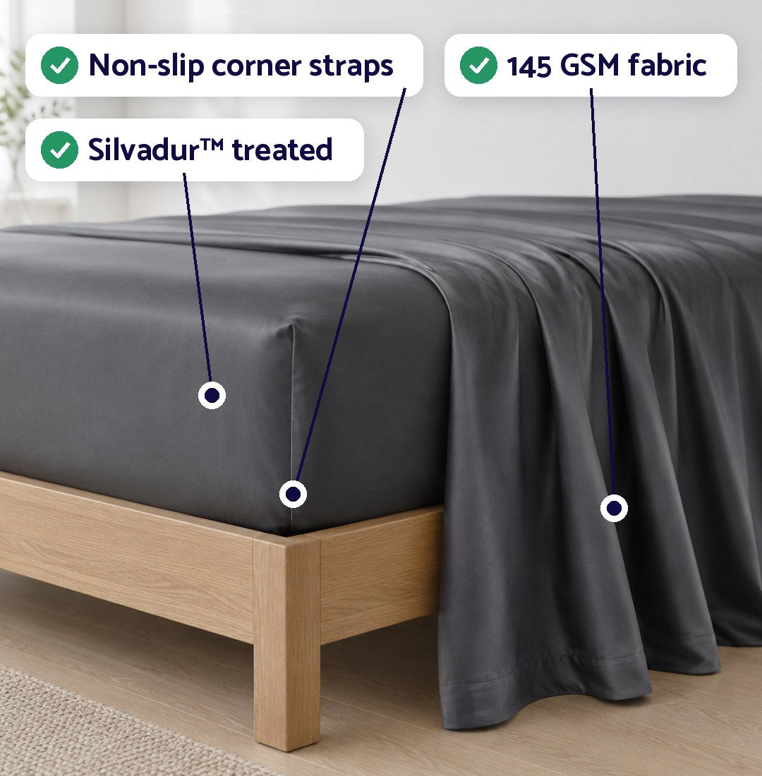 Charcoal Dosaze Luxe sheets on an oak bed, labeled: non-slip corner straps, Silvadur treated, 145 GSM fabric